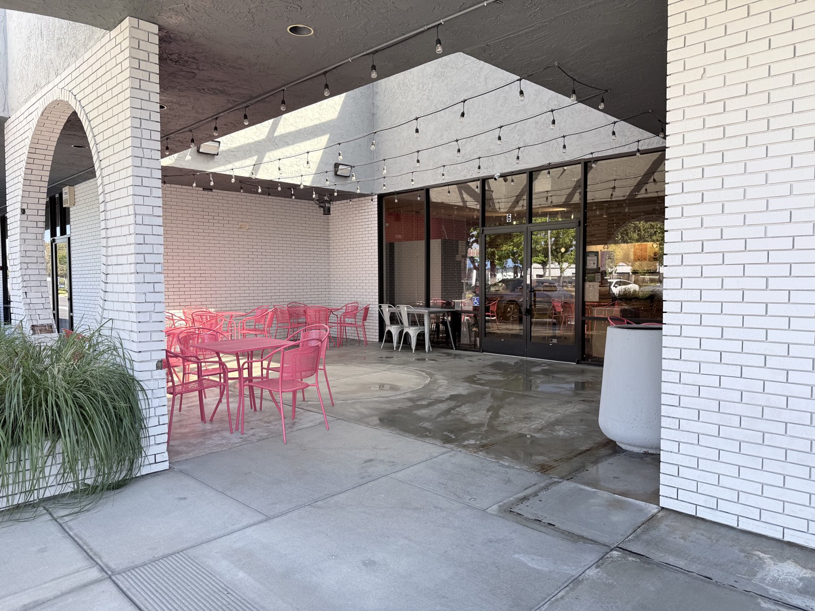 After — storefront entry patio cleaned, pink metal tables and chairs reset on uniform concrete under the string lights