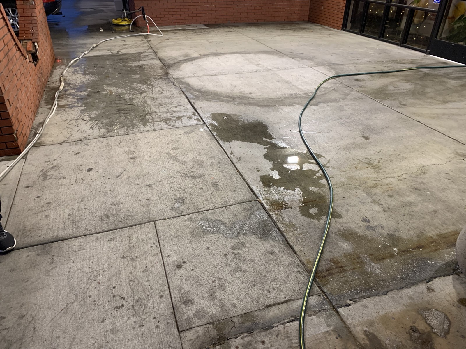 Before — dark buildup and stains across the storefront patio slabs, hoses laid out for the night wash