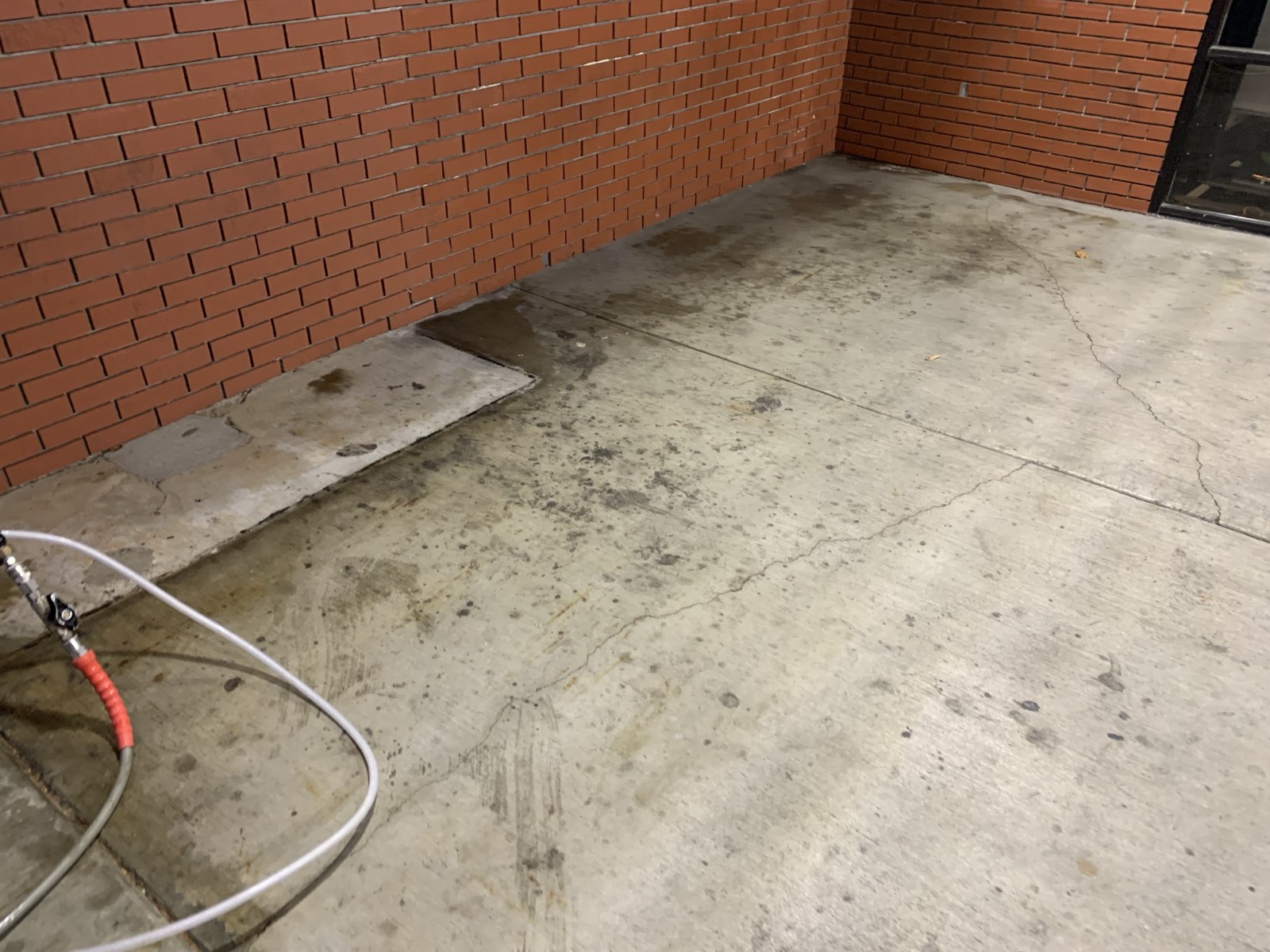 Before — gum spots and embedded grime on the walkway concrete along the red brick wall