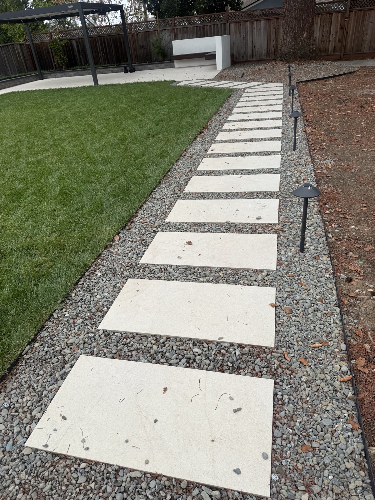After — cleaned cream porcelain stepping pavers set in gravel beside new lawn in a San Jose backyard