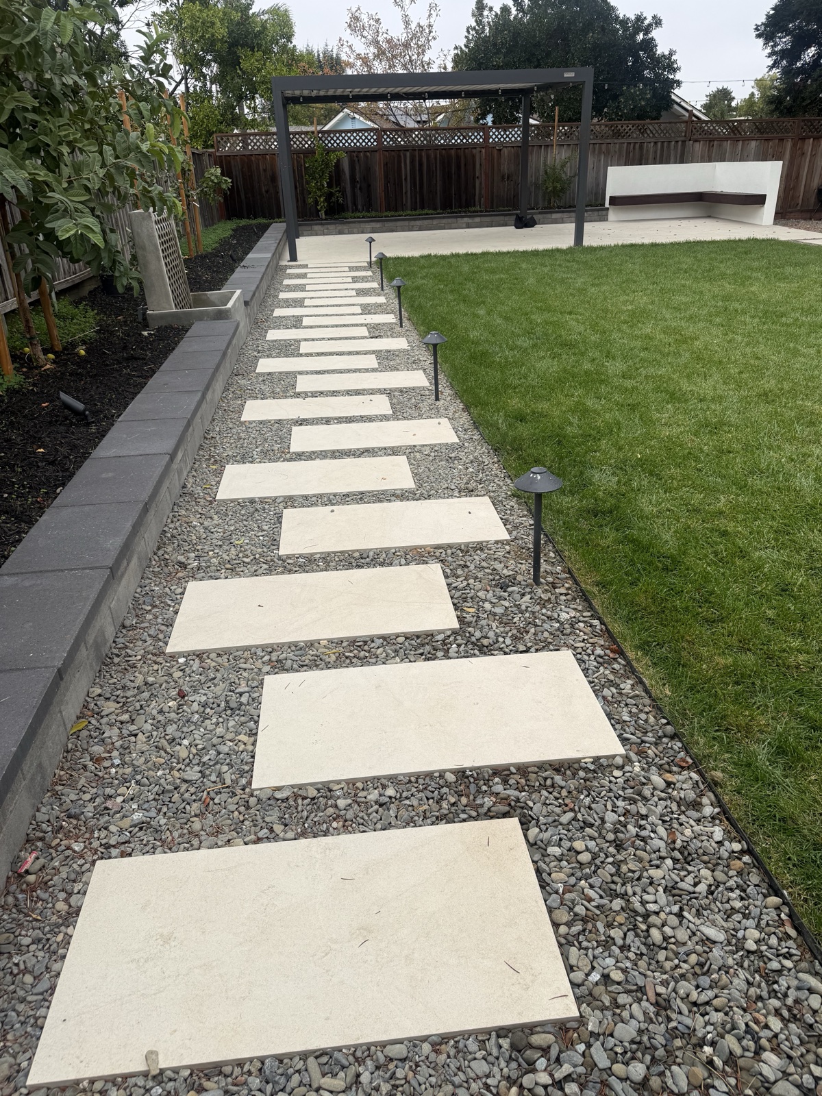 After — porcelain stepping paver walkway cleaned, running between lawn and planting beds toward the pergola