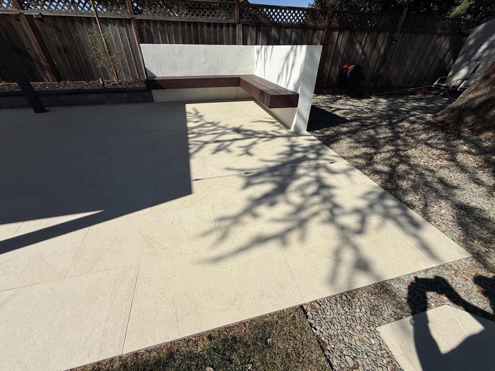 After — large-format porcelain paver patio cleaned and sealed, white seating wall and wood bench behind