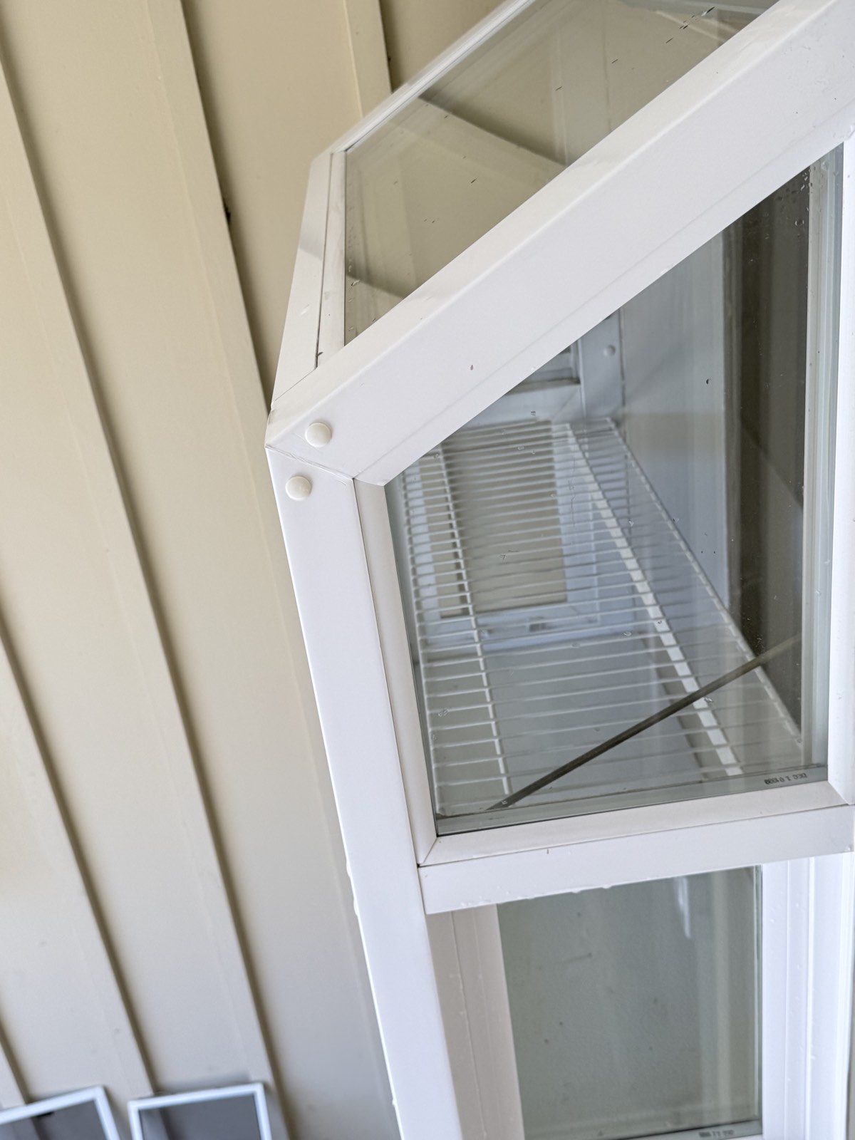After — close-up of a garden window corner with clean glass edges and wiped white frame
